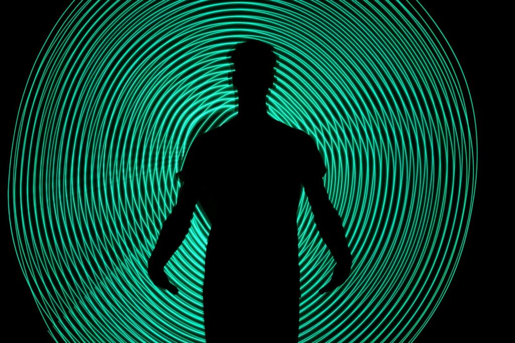 Silhouette of a man standing against dynamic green light swirls. Captivating and abstract art.