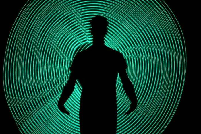 Silhouette of a man standing against dynamic green light swirls. Captivating and abstract art.